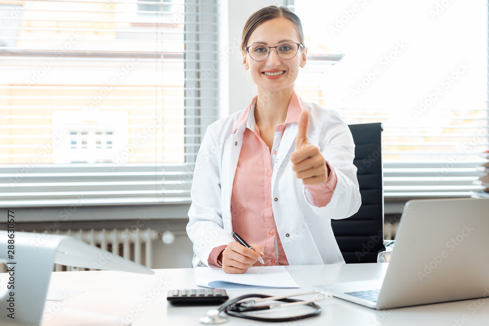 Doctor woman giving thumbs-up sitting on desk in her office Doctor woman giving thumbs-up sitting on desk in her office