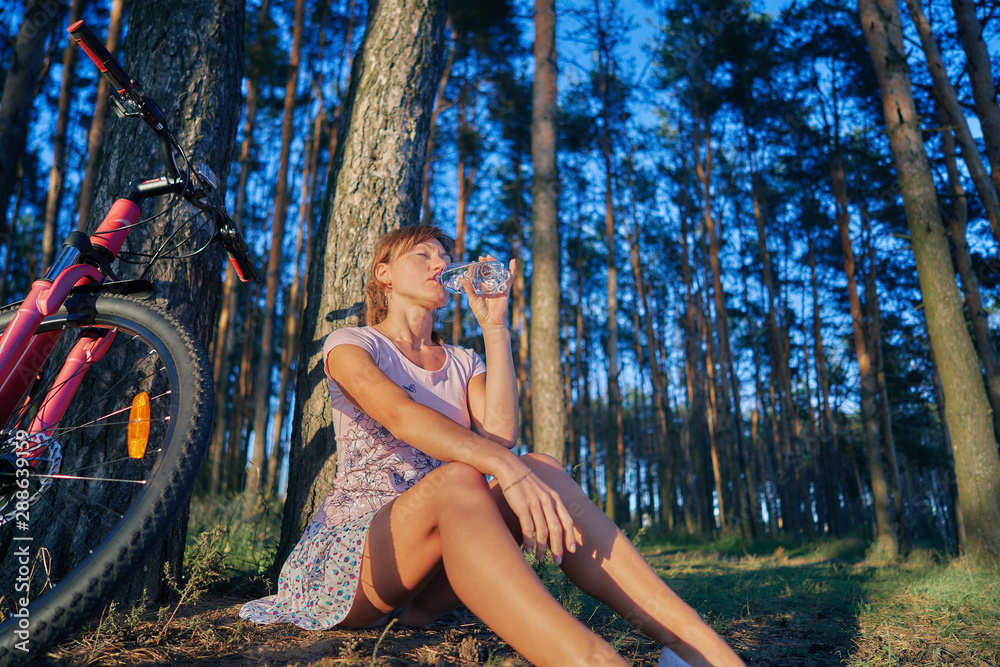 young girl with a bicycle. she rests and drinks water from a bottle. sunset sun. young girl with a bicycle. she rests and drinks water from a bottle. sunset sun.