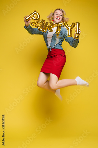 Stock photo portrait of attractive girl with red lips holding shining bright inflatable word HAPPY. Isolate on orange background.