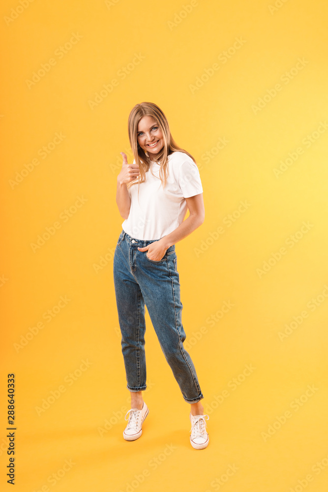 Full length image of nice blond woman wearing casual t-shirt smiling at camera and showing thumb up Full length image of nice blond woman wearing casual t-shirt smiling at camera and showing thumb up