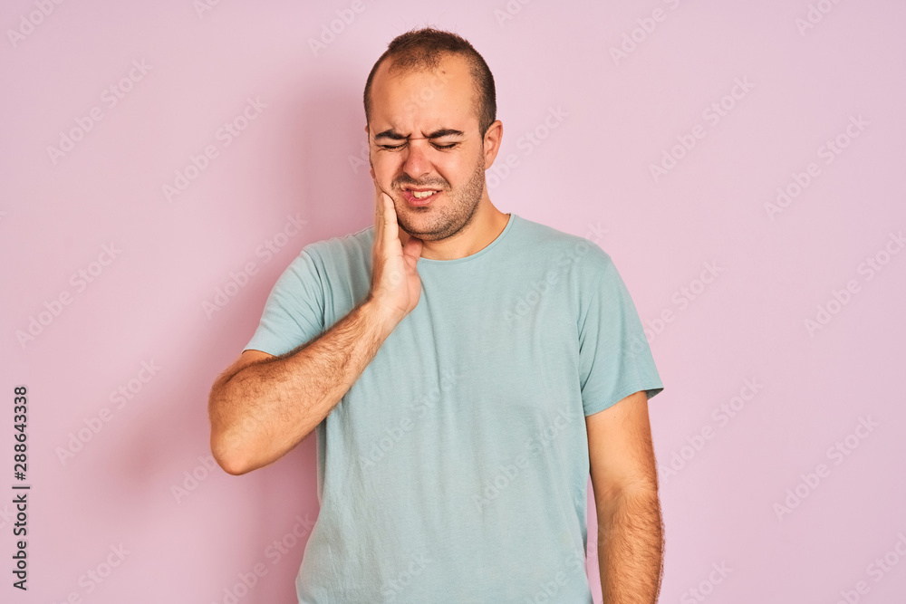 Young man wearing blue casual t-shirt standing over isolated pink background touching mouth with hand with painful expression because of toothache or dental illness on teeth. Dentist concept. Young man wearing blue casual t-shirt standing over isolated pink background touching mouth with hand with painful expression because of toothache or dental illness on teeth. Dentist concept.