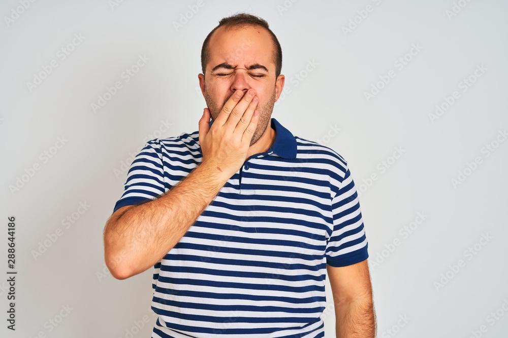Young man wearing casual striped polo standing over isolated white background bored yawning tired covering mouth with hand. Restless and sleepiness. Young man wearing casual striped polo standing over isolated white background bored yawning tired covering mouth with hand. Restless and sleepiness.