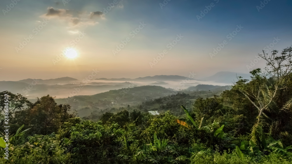 Mountain view panorama misty morning of top hills and green forest around with sea of fog with yellow sun light in the sky background, sunrise at ITTI View Point, Khao Kho, Phetchabun, Thailand.