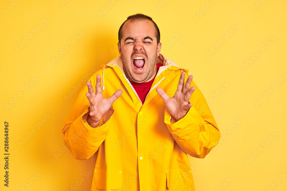 Young man wearing rain coat standing over isolated yellow background celebrating mad and crazy for success with arms raised and closed eyes screaming excited. Winner concept Young man wearing rain coat standing over isolated yellow background celebrating mad and crazy for success with arms raised and closed eyes screaming excited. Winner concept