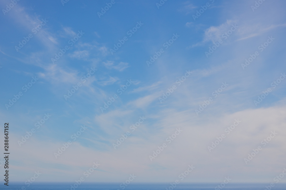 Soft whispy clouds on a blue sky over the ocean.