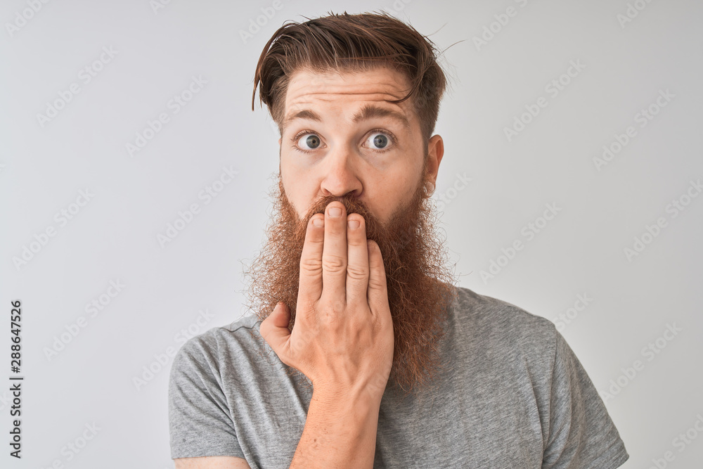 Young redhead irish man wearing t-shirt standing over isolated grey background cover mouth with hand shocked with shame for mistake, expression of fear, scared in silence, secret concept Young redhead irish man wearing t-shirt standing over isolated grey background cover mouth with hand shocked with shame for mistake, expression of fear, scared in silence, secret concept