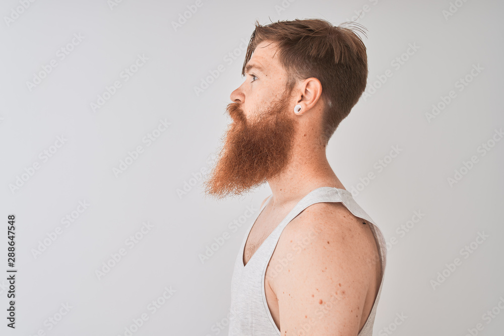 Young redhead irish man wearing t-shirt standing over isolated grey background looking to side, relax profile pose with natural face with confident smile. Young redhead irish man wearing t-shirt standing over isolated grey background looking to side, relax profile pose with natural face with confident smile.