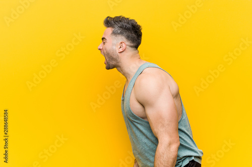 Young fitness man against a yellow background shouting towards a copy space