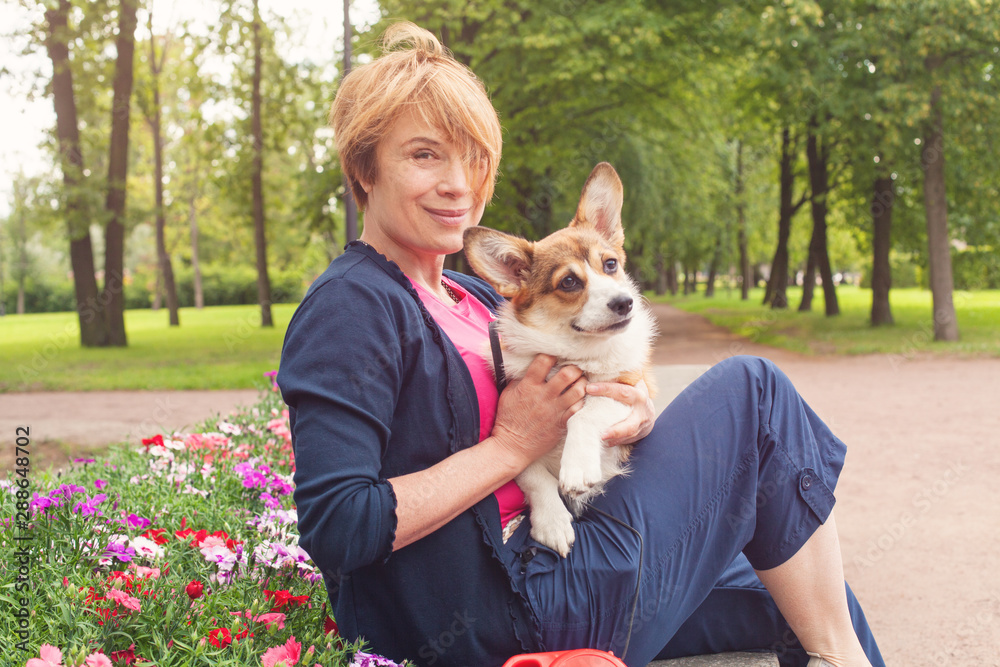 Happy elderly woman sitting with dog on bench in blossom summer park Happy elderly woman sitting with dog on bench in blossom summer park