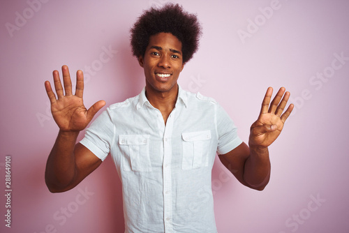 Young american man with afro hair wearing white shirt standing over isolated pink background showing and pointing up with fingers number nine while smiling confident and happy.