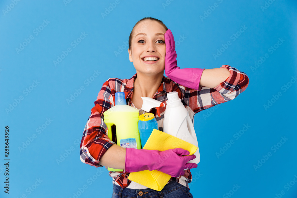 Portrait of happy housewife in rubber gloves holding detergent bottles and washing cleansers while doing housework Portrait of happy housewife in rubber gloves holding detergent bottles and washing cleansers while doing housework