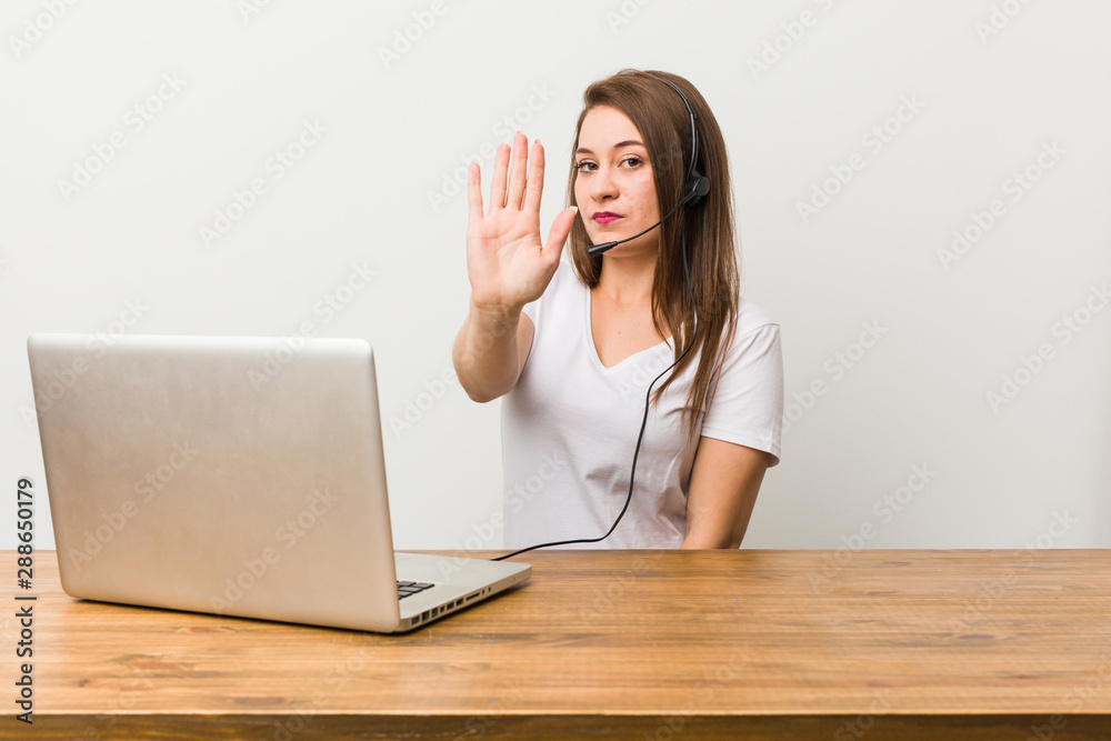 Young telemarketer woman standing with outstretched hand showing stop sign, preventing you.