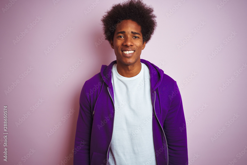 Young african american man wearing purple sweatshirt standing over isolated pink background with a happy and cool smile on face. Lucky person.