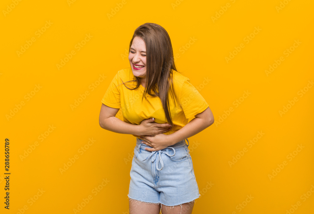 Obraz premium Young woman teenager wearing a yellow shirt laughs happily and has fun keeping hands on stomach.