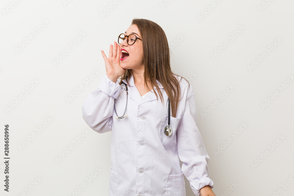 Young doctor woman against a white wall shouting and holding palm near opened mouth. Young doctor woman against a white wall shouting and holding palm near opened mouth.