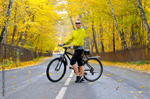 Girl with a bicycle on the road among autumn forest