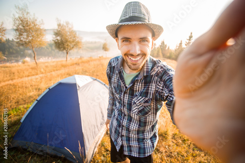 Fanny bearded man smiling and taking selfie in mountains from his smart phone. Traveler man with beard wearing hat take self portrait with camera after autumn hiking. Travel, lifestyle photo