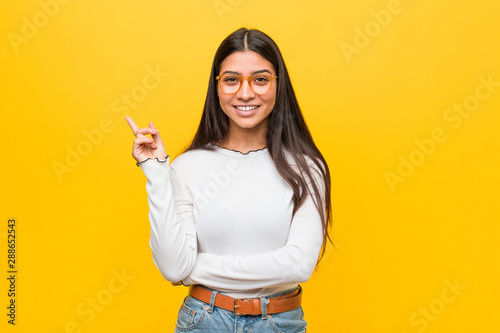 Young pretty arab woman against a yellow background smiling cheerfully pointing with forefinger away.
