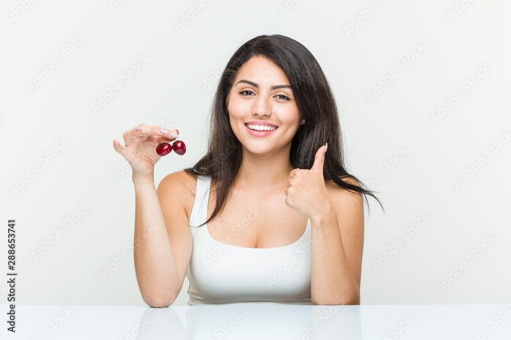 Young hispanic woman holding cherries smiling and raising thumb up Young hispanic woman holding cherries smiling and raising thumb up