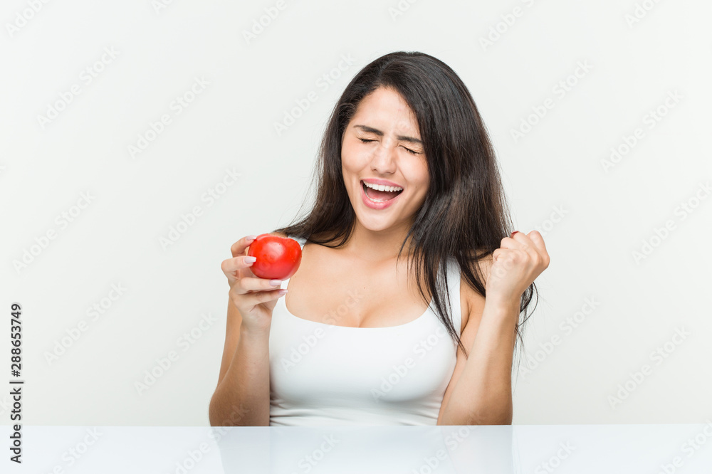 Young hispanic woman holding a tomato cheering carefree and excited. Victory concept. Young hispanic woman holding a tomato cheering carefree and excited. Victory concept.