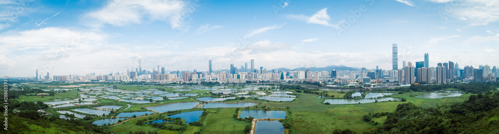 Naklejka premium panorama view of rural green fields with fish ponds between Hong Kong and skylines of Shenzhen,China