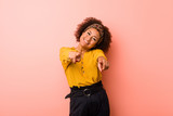 Young african american woman against a pink background cheerful smiles pointing to front.