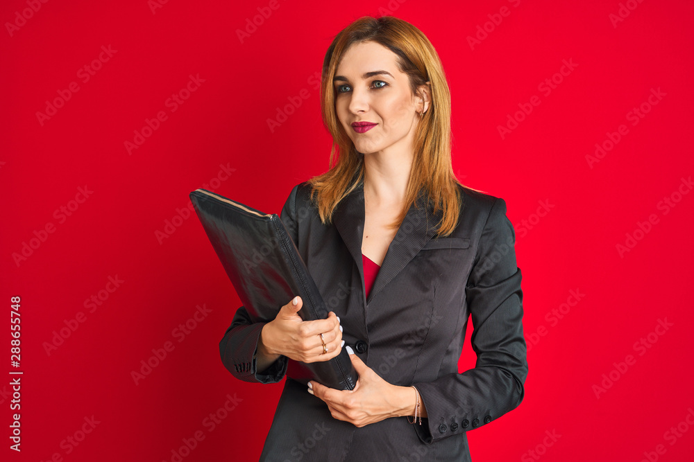 Young beautiful redhead businesswoman wearing suit holding suitcase Young beautiful redhead businesswoman wearing suit holding suitcase