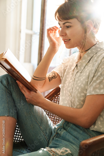 Pretty woman indoors at home sit in chair reading book.