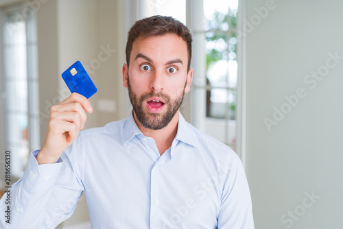 Handsome business man holding credit card scared in shock with a surprise face, afraid and excited with fear expression