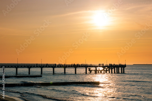 silhouettes of people walking on a pier by the sea against a sunset orange sky