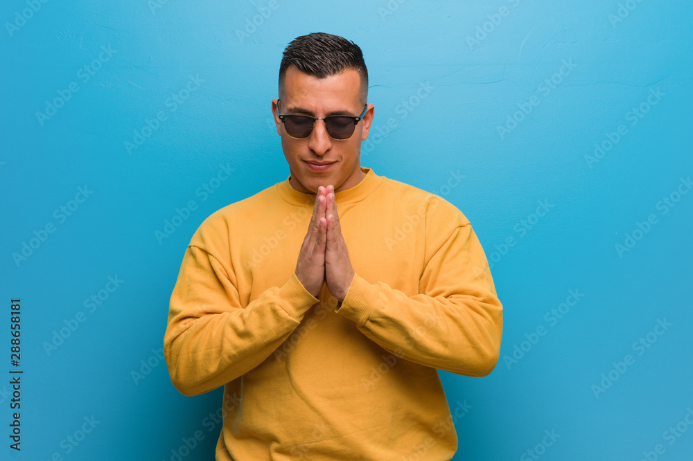 Young colombian man praying very happy and confident