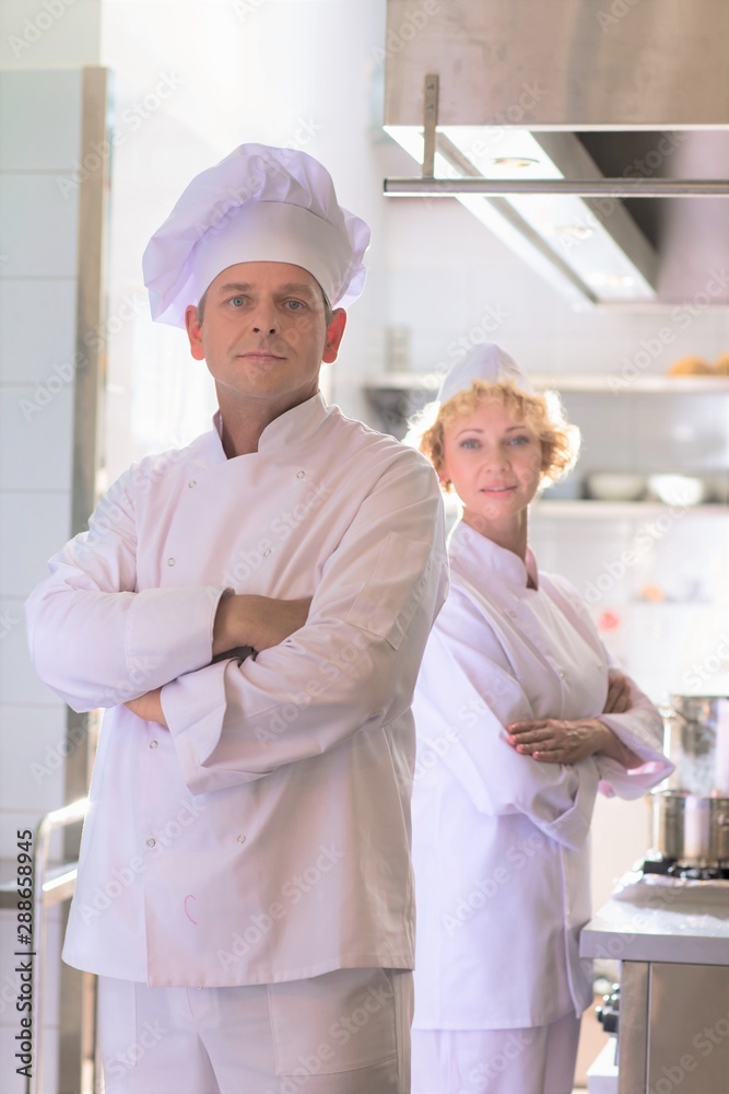 Portrait of confident mature chefs standing with cross arms at kitchen restaurant