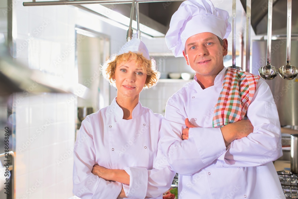 Portrait of confident mature chefs standing with cross arms at kitchen restaurant