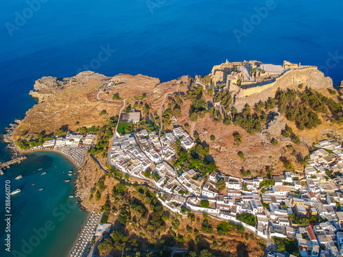Aerial birds eye view drone photo of village Lindos, Rhodes island, Dodecanese, Greece. Sunset panorama with castle, Mediterranean sea coast. Famous tourist destination in South Europe.