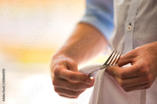 Midsection of young waiter cleaning fork in restaurant