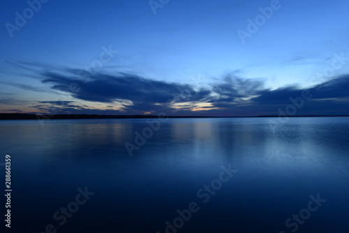 blue sky in the twilight glow from behind clouds over the azure calm surface of the water