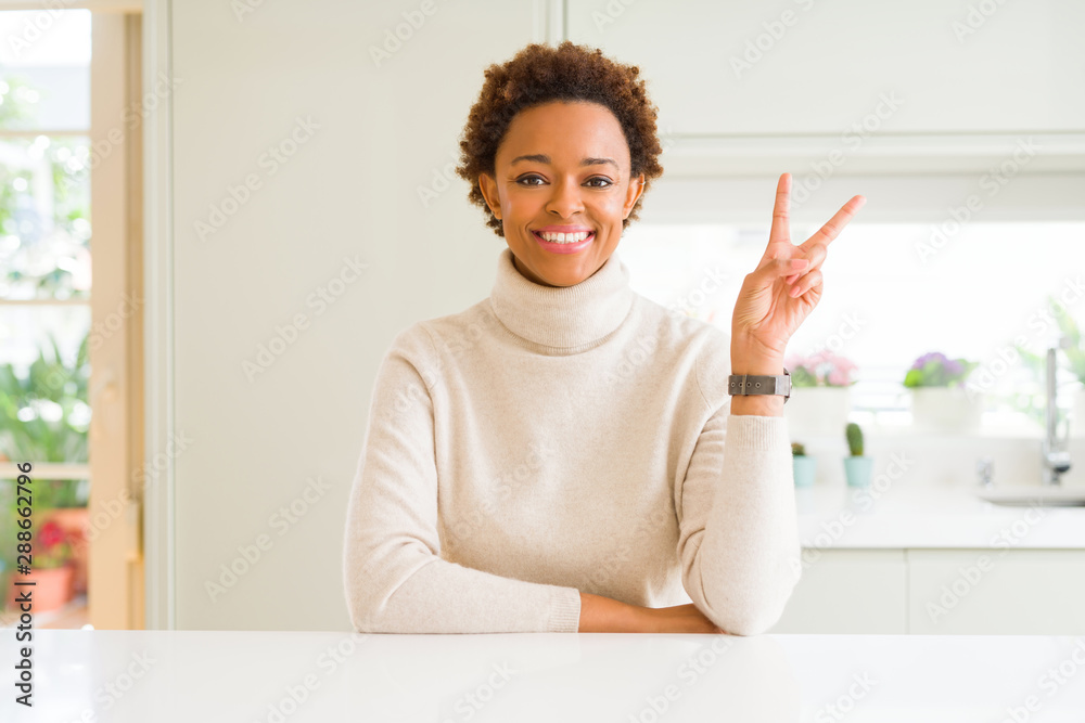 Young beautiful african american woman at home smiling with happy face winking at the camera doing victory sign. Number two.