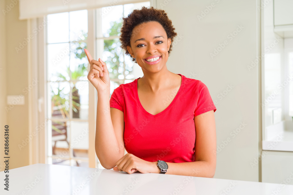 Young beautiful african american woman at home with a big smile on face, pointing with hand and finger to the side looking at the camera. Young beautiful african american woman at home with a big smile on face, pointing with hand and finger to the side looking at the camera.