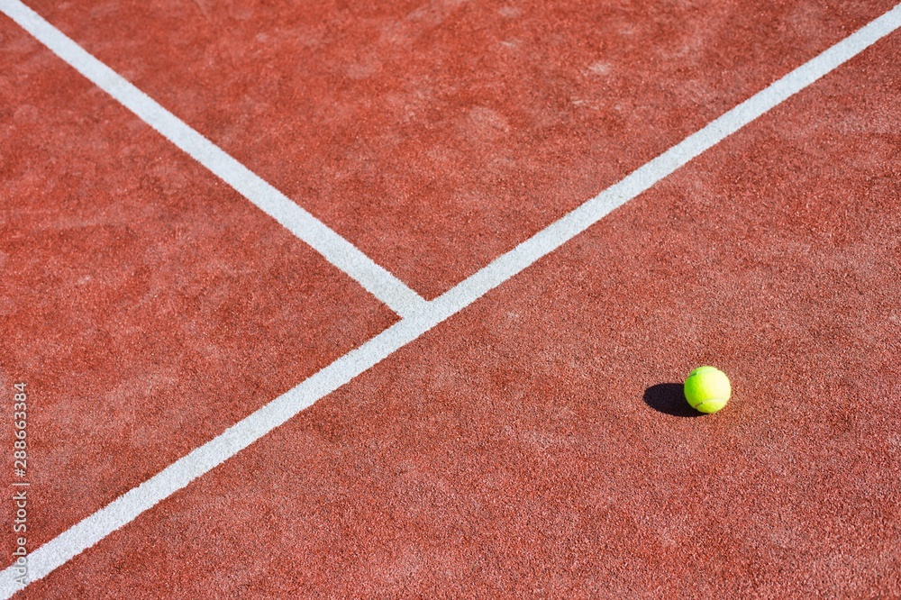Tennis ball on red court during sunny day