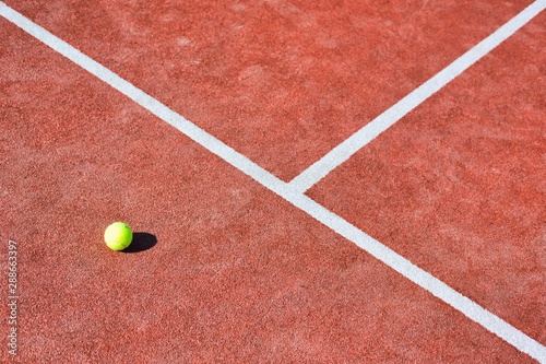 Tennis ball on red court during sunny day © moodboard