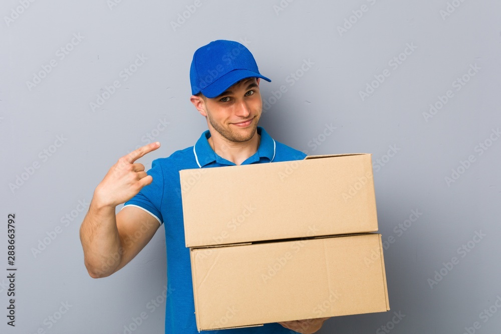 Young man delivering packages pointing with finger at you as if inviting come closer. Young man delivering packages pointing with finger at you as if inviting come closer.