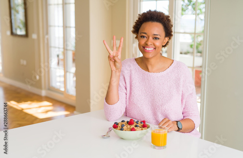Young african american woman having healthy breakfast in the morning at home showing and pointing up with fingers number three while smiling confident and happy.