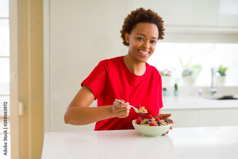 Young beautiful african american woman with afro hair eating healthy wholemeal cereals and berries as healthy breakfast