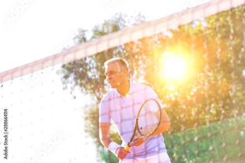 Mature man playing tennis at court with yellow lens flare in background