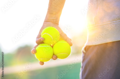 Photo of senior man holding tennis balls on court with yellow lens flare in background © moodboard