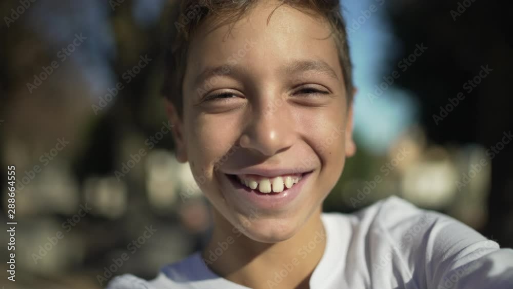 Cute boy smiling happily at camera while he's taking selfies in a sunny day in the city or in the park in spring or summer. Cute boy smiling happily at camera while he's taking selfies in a sunny day in the city or in the park in spring or summer.