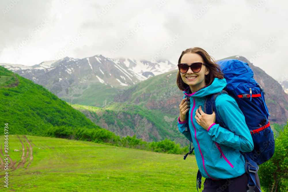 Naklejka premium Cheerful women with backpack traveling in mountain. Joyful female traveler with sunglasses smile and looking at camera