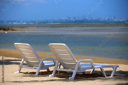 Two white chairs standing on the beach in front the sea.