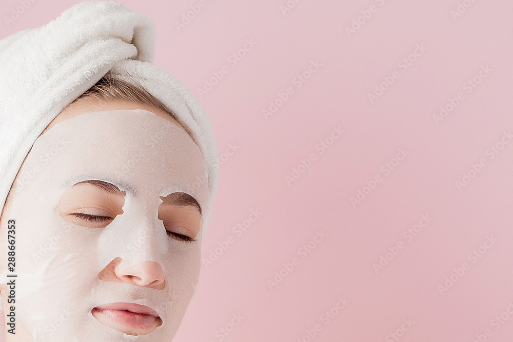 Beautiful young woman is applying a cosmetic tissue mask on a face on a pink background. Healthcare and beauty treatment and technology concept