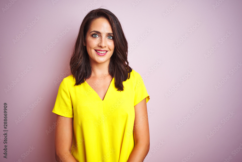 Young beautiful woman wearing yellow t-shirt standing over pink isolated background with a happy and cool smile on face. Lucky person. Young beautiful woman wearing yellow t-shirt standing over pink isolated background with a happy and cool smile on face. Lucky person.